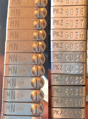 multiple small metal nues tags showing front and backside with MN imprinted on one side and an ID number printed on the other
